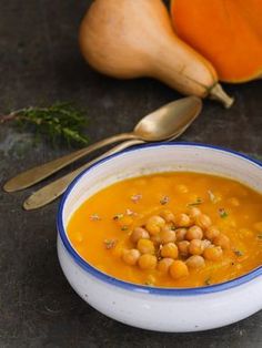 a bowl of soup with chickpeas and carrots next to some spoons