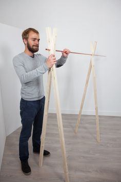 a man standing in front of a wooden easel holding a stick with one hand