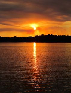 the sun is setting over water with trees in the background