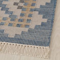 a blue and white rug with fringes on top of wooden floor next to wall