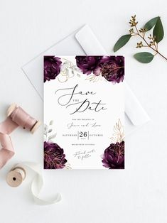 a wedding card with purple flowers and greenery on the front, next to a pair of scissors