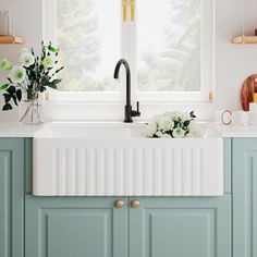 a kitchen with blue cabinets and white flowers in vases on the window sill