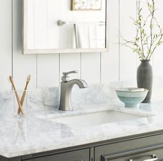 a bathroom sink sitting under a mirror next to a vase with a plant in it