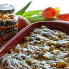 a casserole dish with cheese and fruit on the side next to tulips