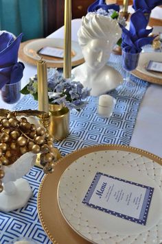 the table is set with blue flowers and gold plates, napkins and place settings