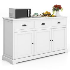 a microwave oven sitting on top of a white cabinet next to a bowl of fruit