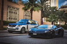 two cars parked next to each other in front of a building with palm trees and tall buildings