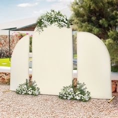 an arch with flowers and greenery on it in the middle of graveled area