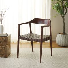 a wooden chair sitting on top of a rug next to a potted plant in front of a window