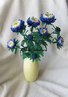 a yellow vase filled with blue and white flowers on top of a white cloth covered bed