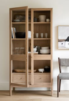 a wooden bookcase with glass doors and drawers in the front, next to a chair