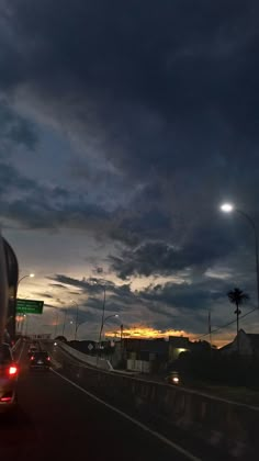 cars driving down the highway at night time with clouds in the sky and street lights