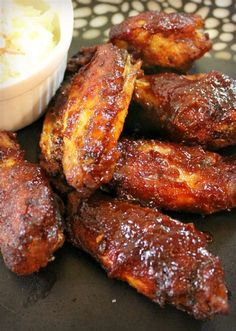 some chicken wings are on a black plate next to a small bowl of ice cream