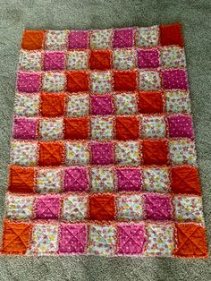 an orange and pink patchwork quilt on the floor with white carpet in front of it