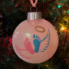 a pink ornament hanging from a christmas tree with an angel foot on it