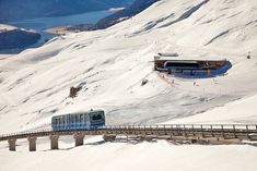 a train traveling over a bridge on top of snow covered ground with mountains in the background