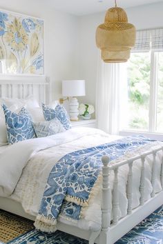 a white bed with blue and white comforter in a bedroom next to a window