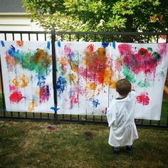 a little boy standing in front of a painting on the side of a metal fence