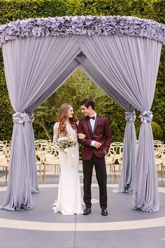 a bride and groom standing under an outdoor wedding ceremony arch with purple flowers on it