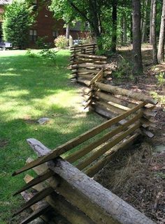 a fence made out of logs in the middle of a yard with grass and trees