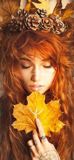 a woman with long red hair wearing a crown and holding a leaf in front of her face