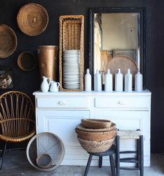 a white dresser topped with baskets next to a mirror