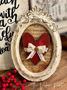 an old frame with a red heart in it and some berries on the table next to it