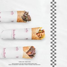 three sub sandwiches are wrapped in paper on a checkered tablecloth with the same image