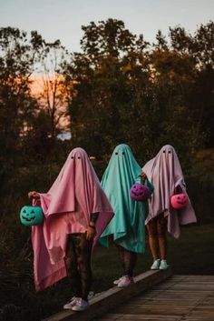 three people dressed in pink, blue and green are standing on a wooden bridge with their faces covered