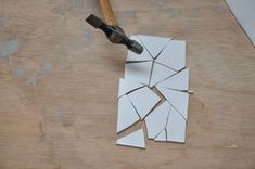 a piece of broken tile with a hammer on it next to some pieces of paper