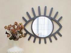 a vase with flowers in it and a mirror on the wall behind it that is shaped like an eye