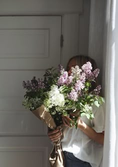 a woman holding a bouquet of flowers in front of a garage door with the curtains open