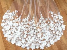 a wedding veil with white flowers on the bottom is laying on top of a wooden floor