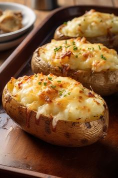 three baked potatoes with cheese and herbs on a wooden tray next to a white plate