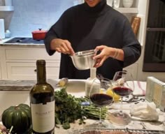 a woman pouring wine into a glass on top of a kitchen counter next to bottles of wine