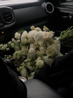 a bouquet of white flowers sitting in the passenger seat of a car with someone holding it