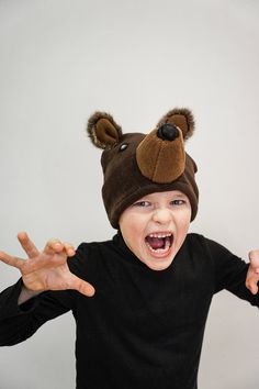 a young boy wearing a brown bear hat and making the peace sign with his hands