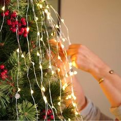 a woman is decorating a christmas tree with lights