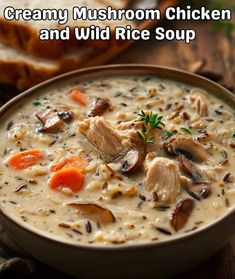 a bowl of creamy mushroom chicken and wild rice soup with bread in the background on a wooden table