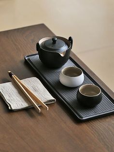 a wooden table topped with two bowls and chopsticks next to a black pot