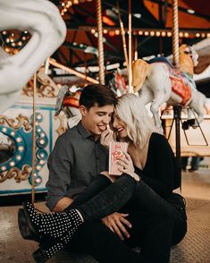 a man and woman sitting on the ground in front of a carousel