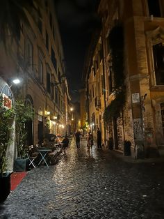 people are walking down the cobblestone street in an old european city at night