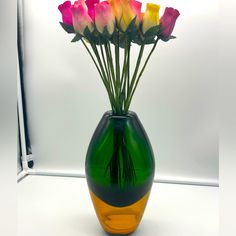 a green vase with pink and yellow roses in it