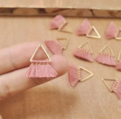 small pink tasseled triangle and triangle shaped studs in gold tone setting on wooden surface