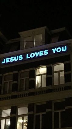 there is a building that has a neon sign on it's side and the words jesus loves you are lit up at night