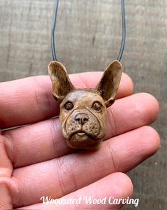 a hand holding a small dog head pendant on a leather cord necklace that says woodard wood carving