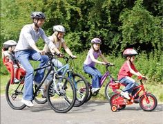 three people riding bikes with two children in the front and one on the back, both wearing helmets