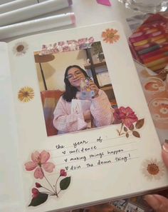 a woman is holding up a photo album with flowers and words on the front cover