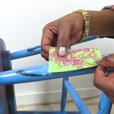 two hands holding a piece of paper on top of a blue wooden chair with pink and yellow designs