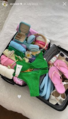 an open suitcase filled with lots of clothes and sandals on top of a bed next to a pillow